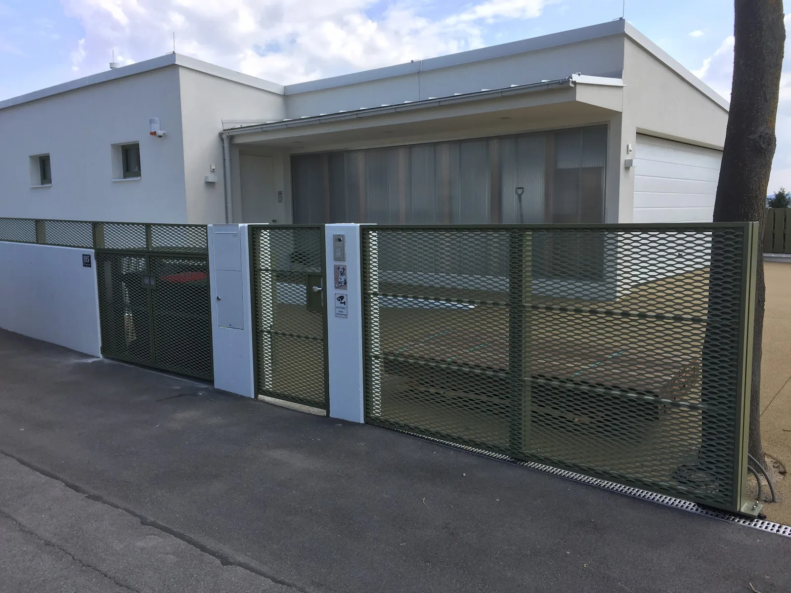 Einfahrtstor und Zaun mit Füllung aus Streckmetall vor einem Flachdachhaus