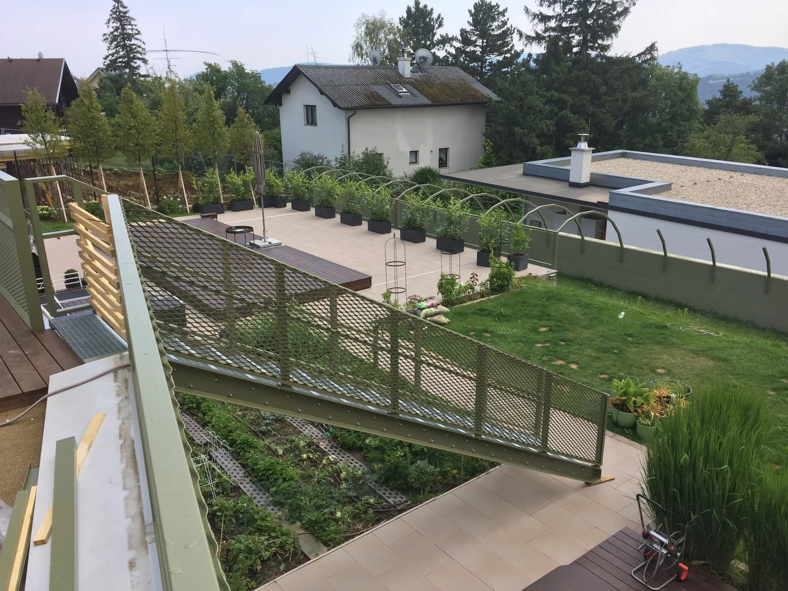 Zaun mit Gitterfüllung rund um Terrasse und Garten, im Hintergrund Bäume und ein Haus