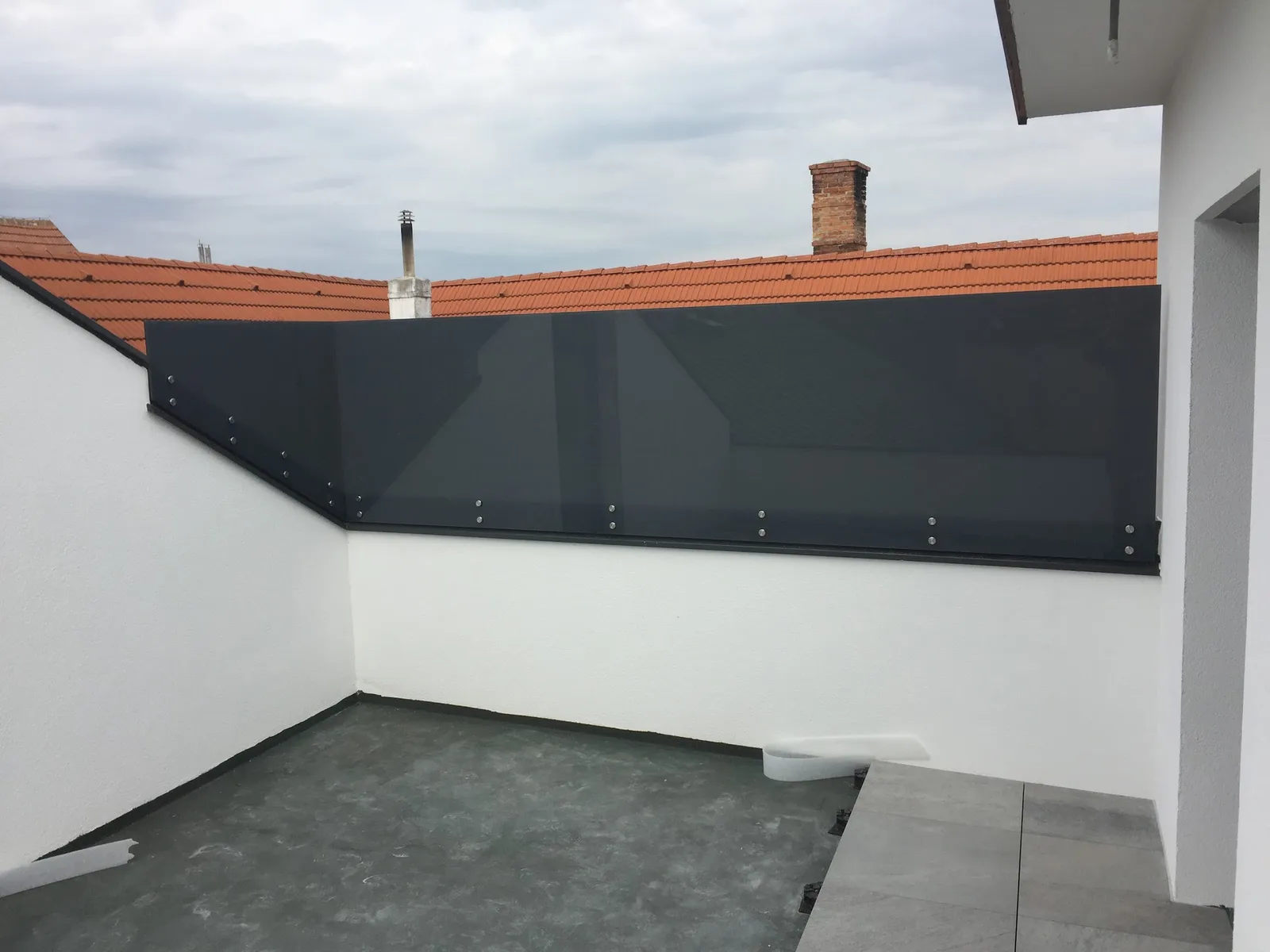 Dunkle Sichtschutzwand als Brüstung auf einer Dachterrasse, dahinter Ziegeldächer