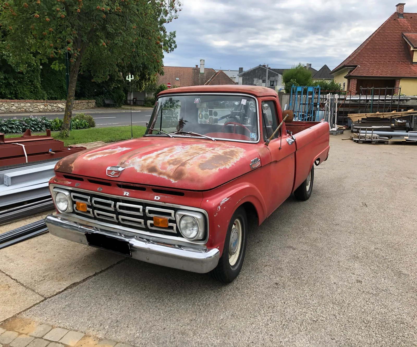 Roter Ford Pick-up von vorne auf dem Betriebsgelände, im Hintergrund gelagertes Material